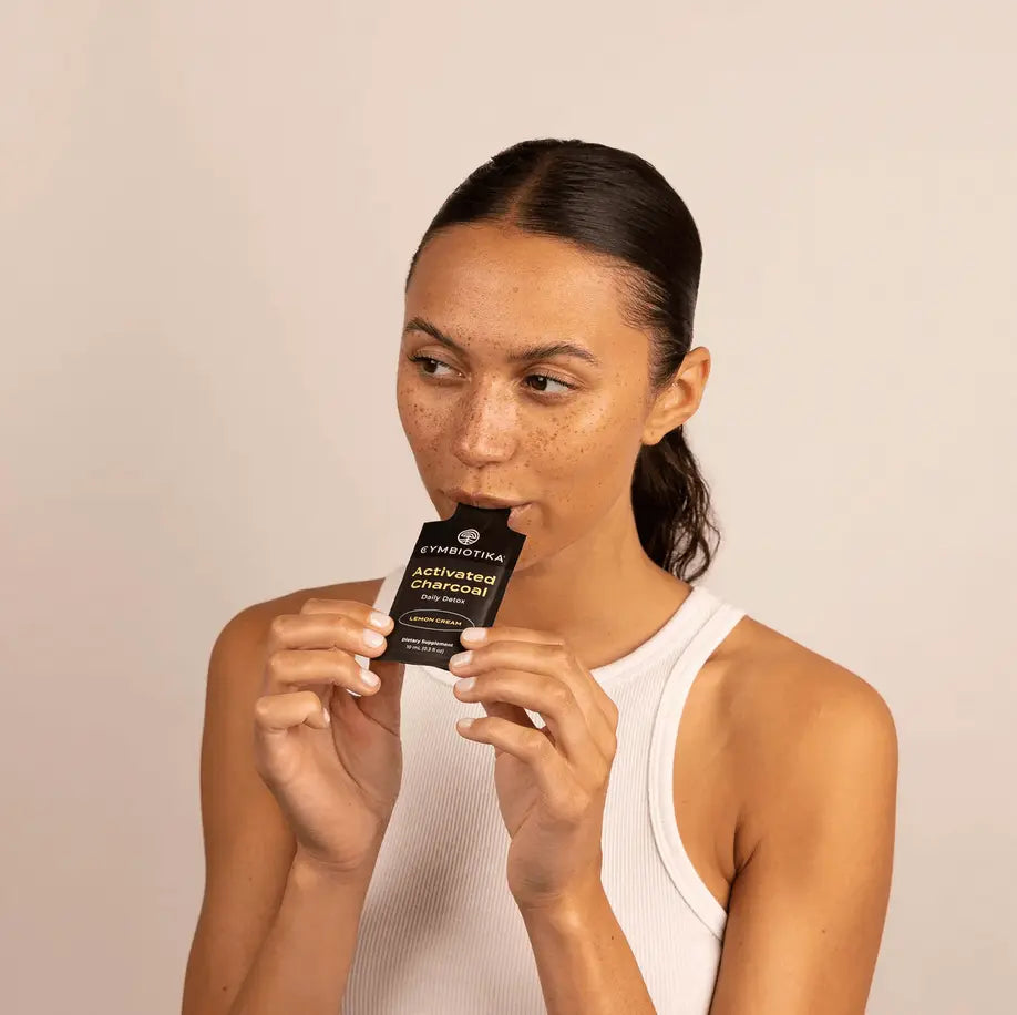 A woman holds Cymbiotika’s Activated Charcoal packet, showcasing its detoxifying benefits.