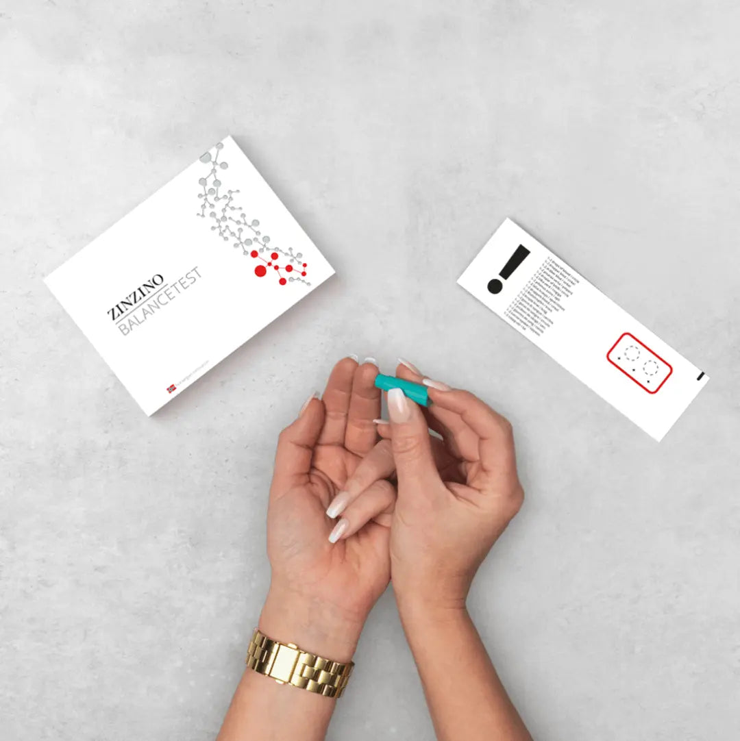 Hands holding a testing device above Zinzino BalanceTest kit on a gray surface.